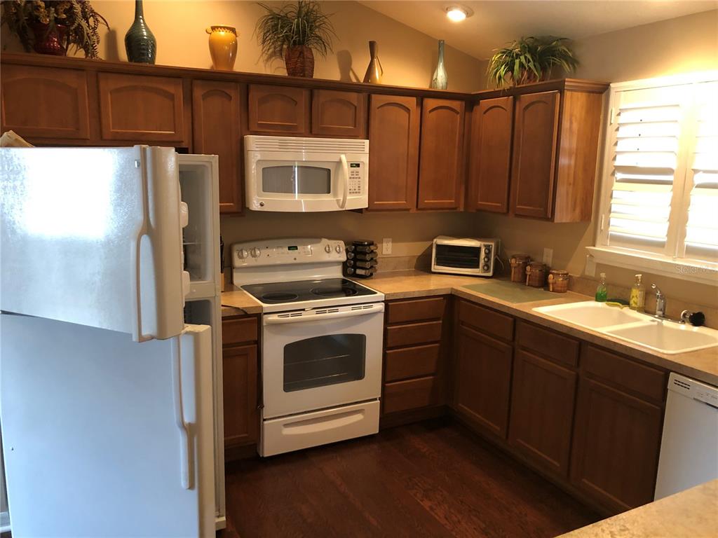 A kitchen features wood cabinets, white appliances, laminate countertops, and dark wood flooring — 308 VIDALIA PLACE, THE VILLAGES, FL