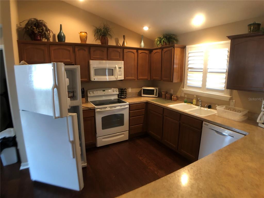 A kitchen features wood cabinets, white appliances, dark flooring, and a double sink — 308 VIDALIA PLACE, THE VILLAGES, FL