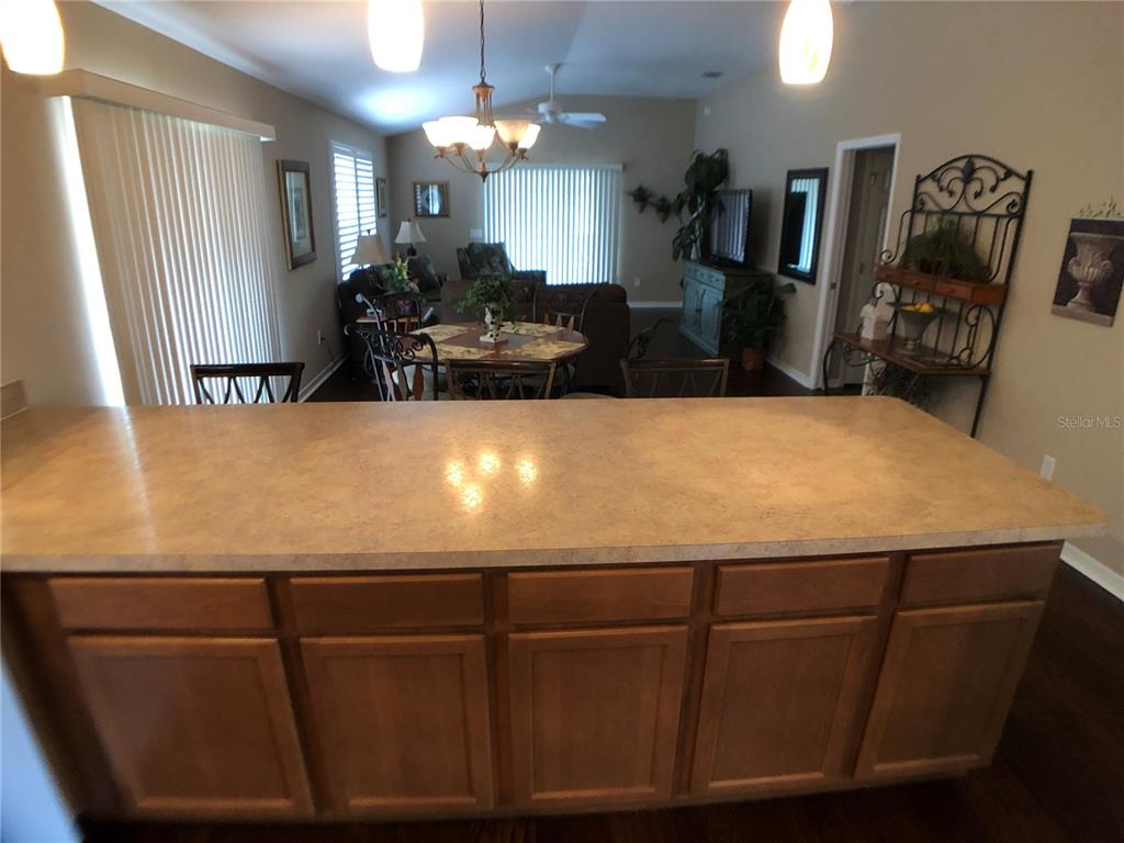 A kitchen island with a tan countertop faces a dining area and living room — 308 VIDALIA PLACE, THE VILLAGES, FL