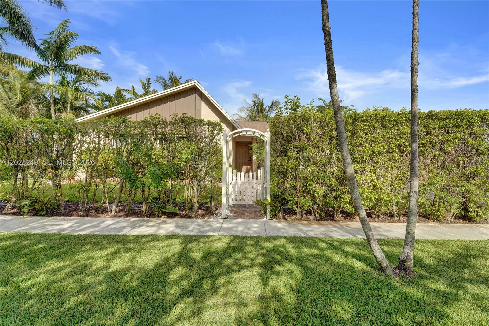A white arched gate leads to a house entrance behind a tall green hedge — 417 SE 4th St, Dania Beach FL 33004, DANIA BEACH, FL