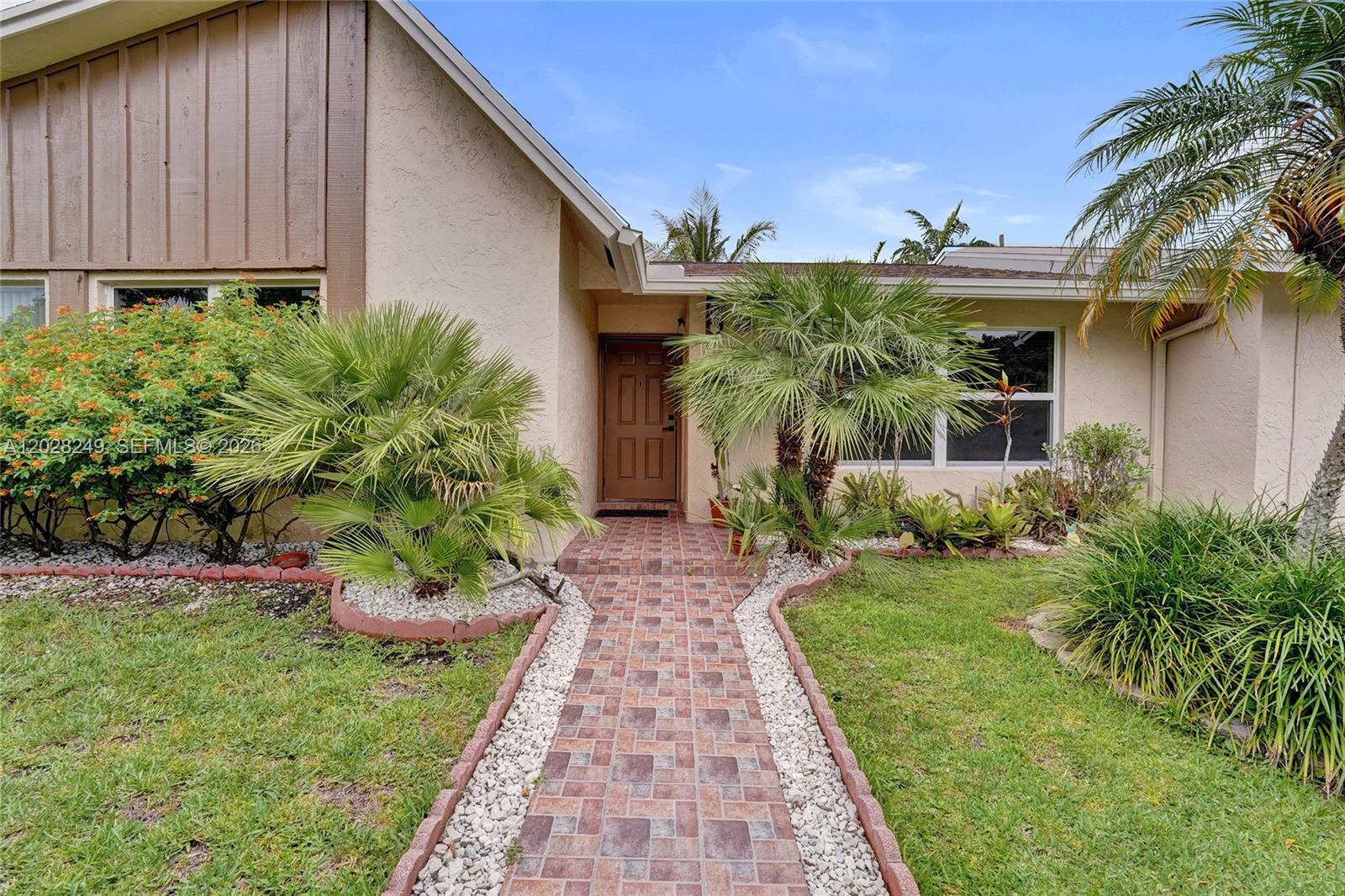 A brick walkway leads to the front entrance of a house with beige stucco siding — 417 SE 4th St, Dania Beach FL 33004, DANIA BEACH, FL