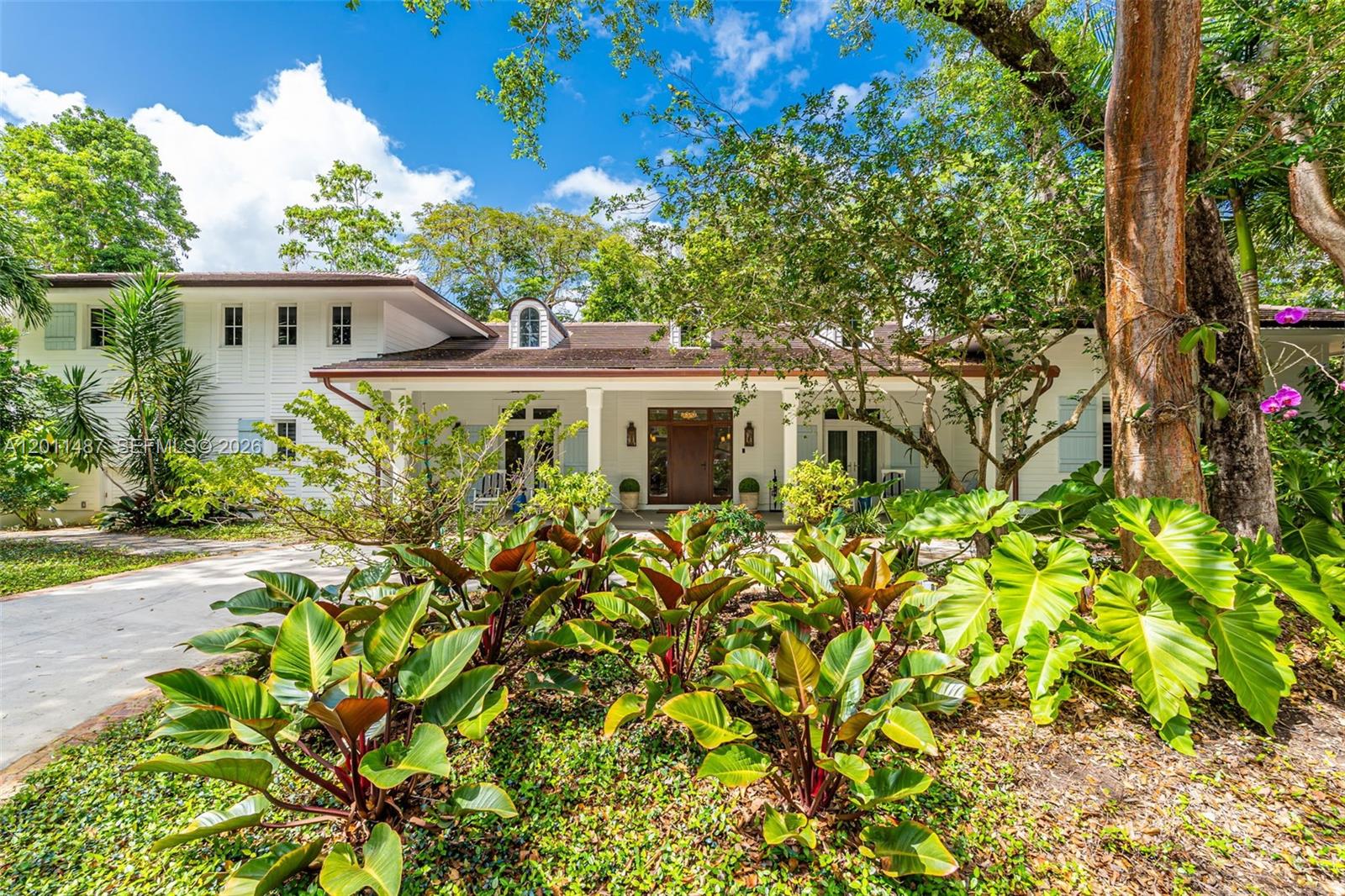 A white two-story house with a covered porch is surrounded by lush tropical landscaping — 4901 Hammock Park Dr, Coral Gables FL 33156, CORAL GABLES, FL