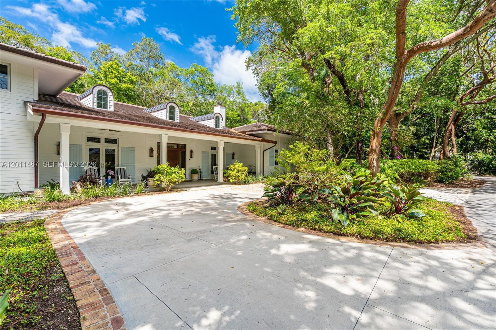 A white house with a covered porch and arched dormers sits beside a circular driveway — 4901 Hammock Park Dr, Coral Gables FL 33156, CORAL GABLES, FL