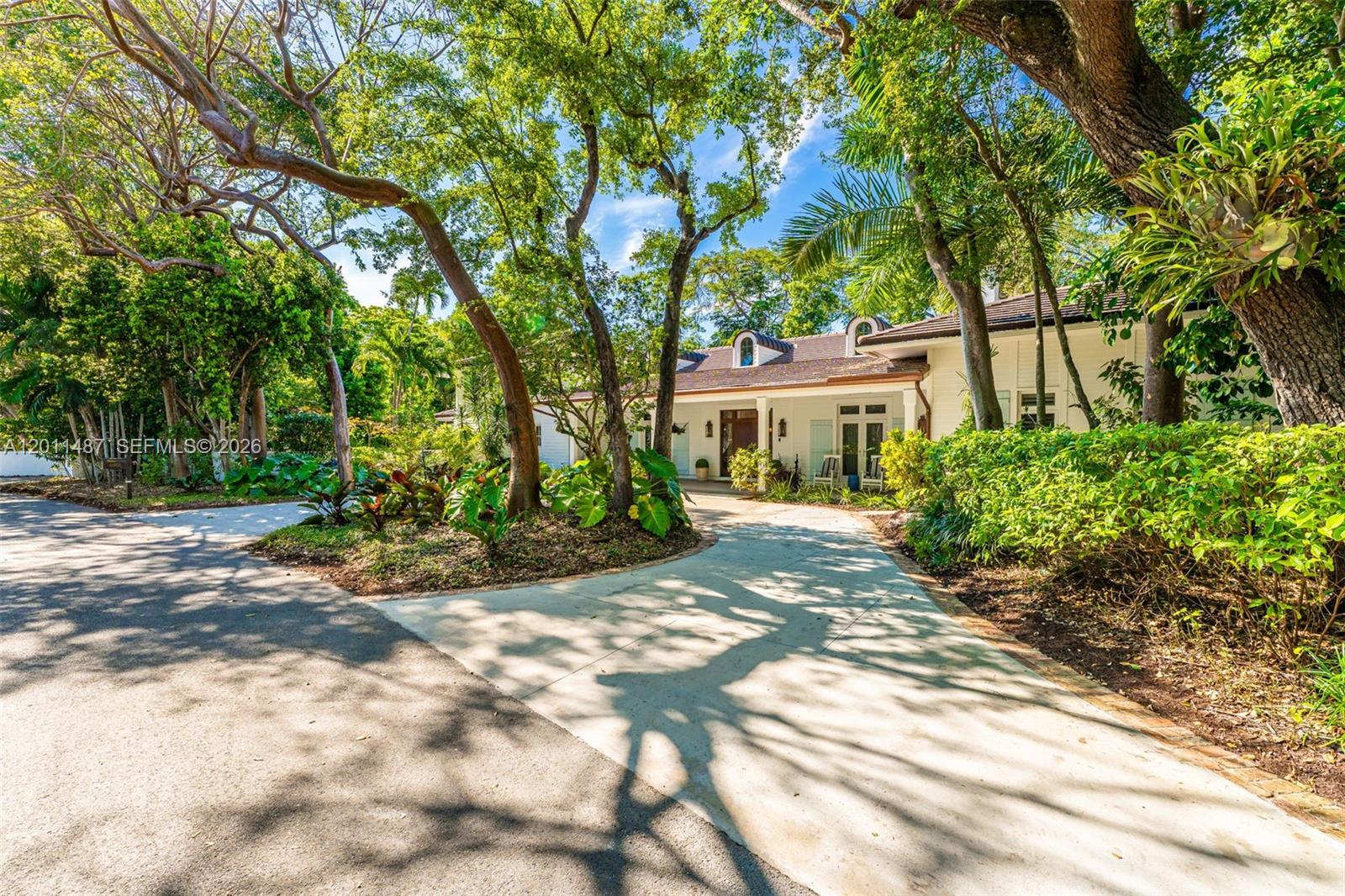 A white house with a concrete driveway is surrounded by lush trees and landscaping — 4901 Hammock Park Dr, Coral Gables FL 33156, CORAL GABLES, FL