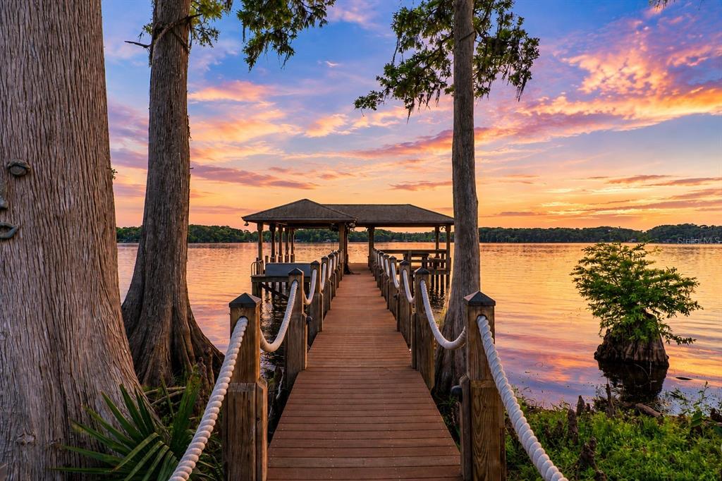 A wooden dock with a covered boat slip extends into a lake at sunset — 746 LAKE MILLS ROAD, OVIEDO, FL
