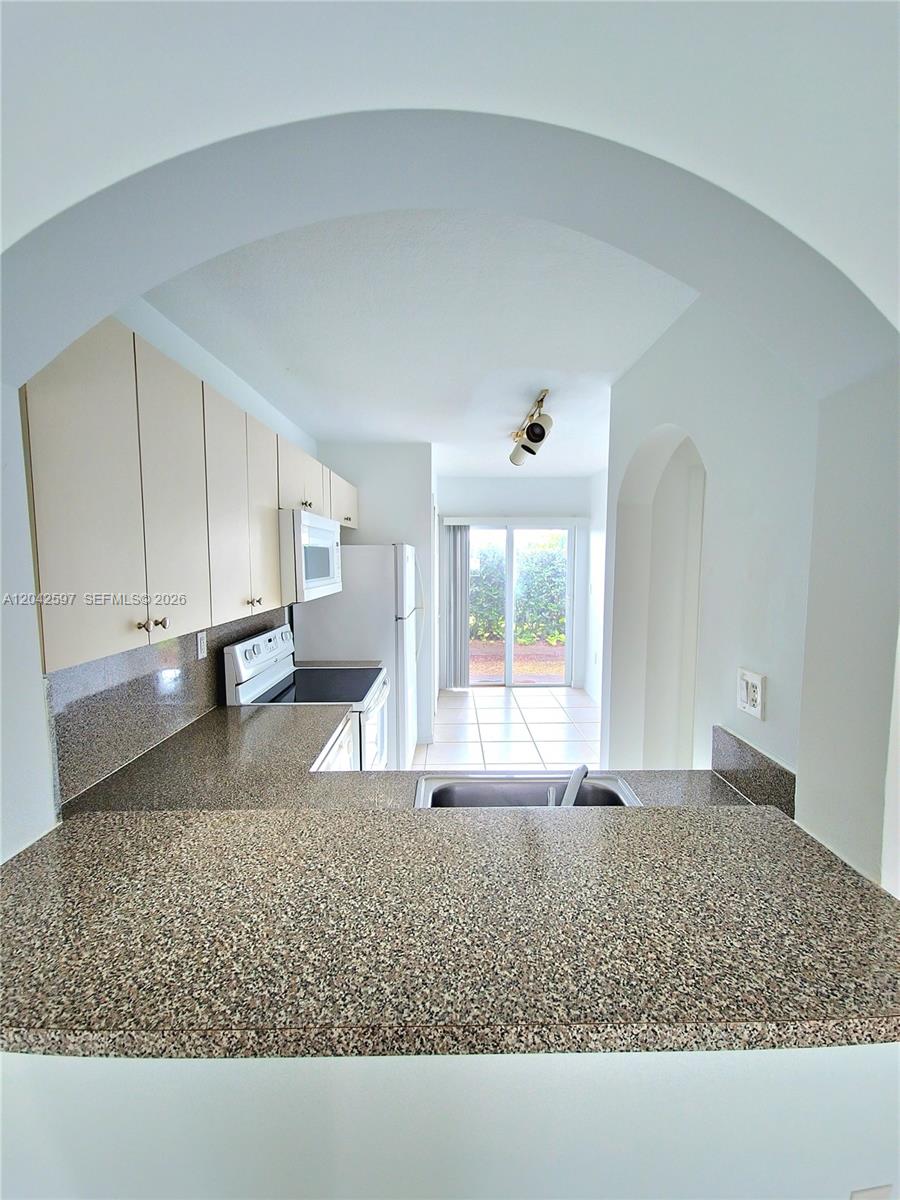 A kitchen features granite countertops, white cabinets, and a pass-through window looking toward sliding doors — 940 NE 33rd Ter # 102, Homestead FL 33033, HOMESTEAD, FL