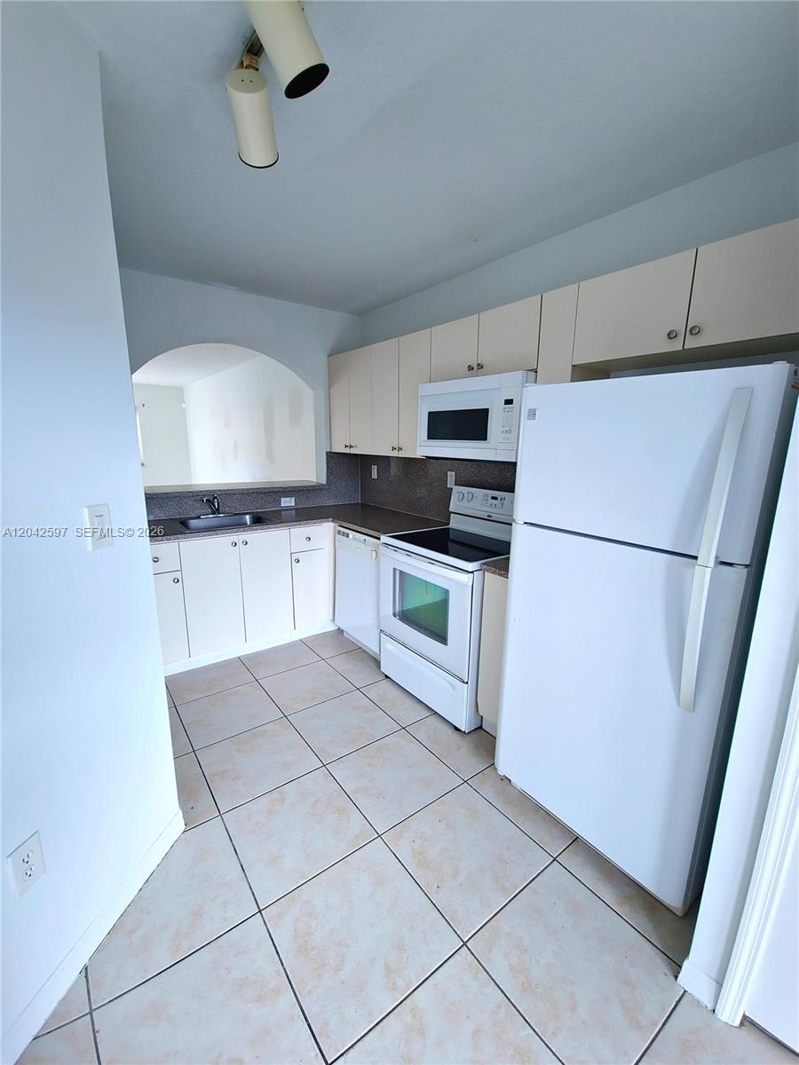 A kitchen features white cabinets, white appliances, a double sink, and light-colored tile flooring — 940 NE 33rd Ter # 102, Homestead FL 33033, HOMESTEAD, FL