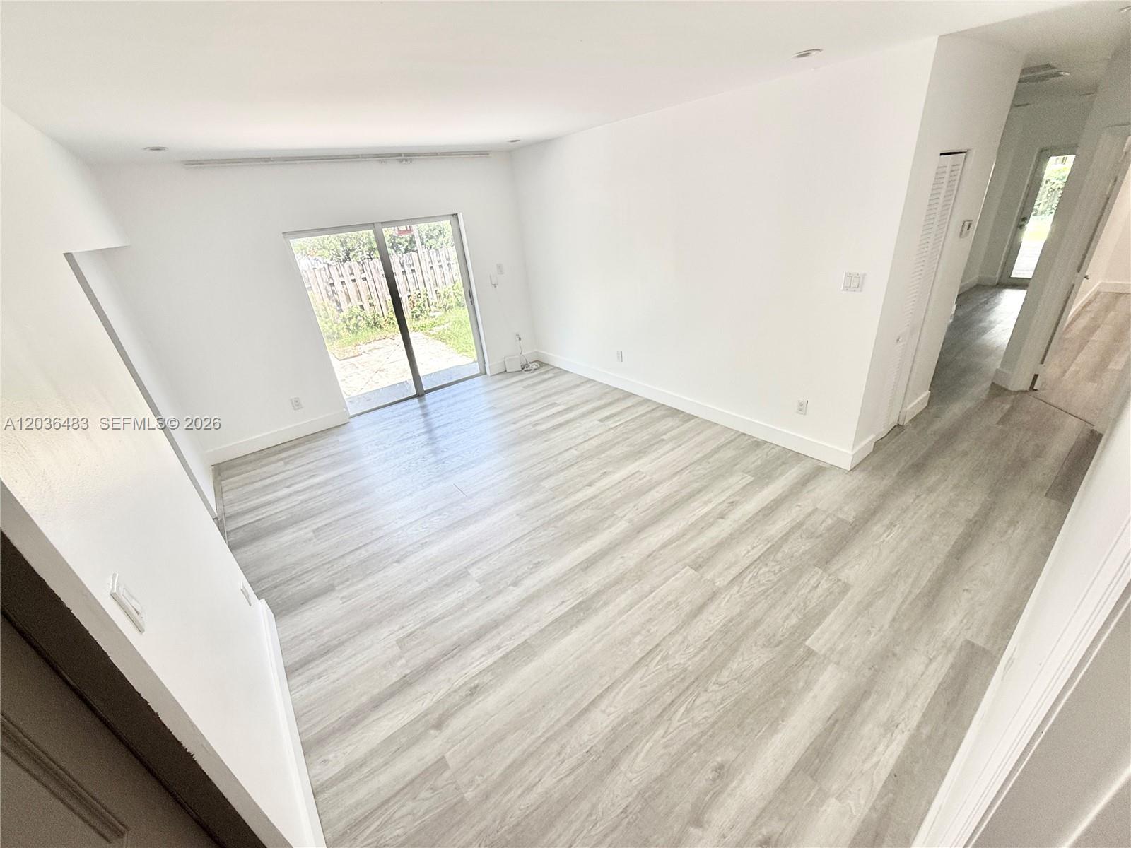 An empty room features light wood-look flooring, white walls, and a sliding glass door — 1272 NE 145th St, Miami FL 33161, MIAMI, FL