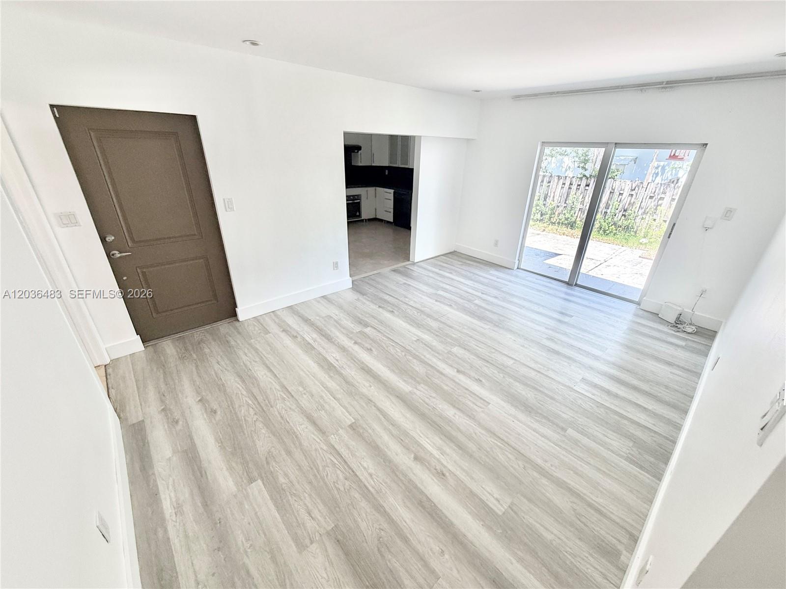 A living room features light wood-look flooring, white walls, a brown door, and sliding glass doors — 1272 NE 145th St, Miami FL 33161, MIAMI, FL