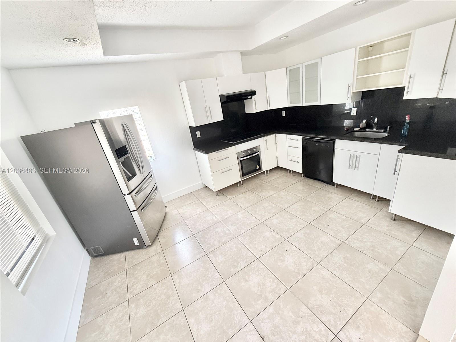 A kitchen features white cabinets, black countertops, stainless steel appliances, and light-colored floor tiles — 1272 NE 145th St, Miami FL 33161, MIAMI, FL