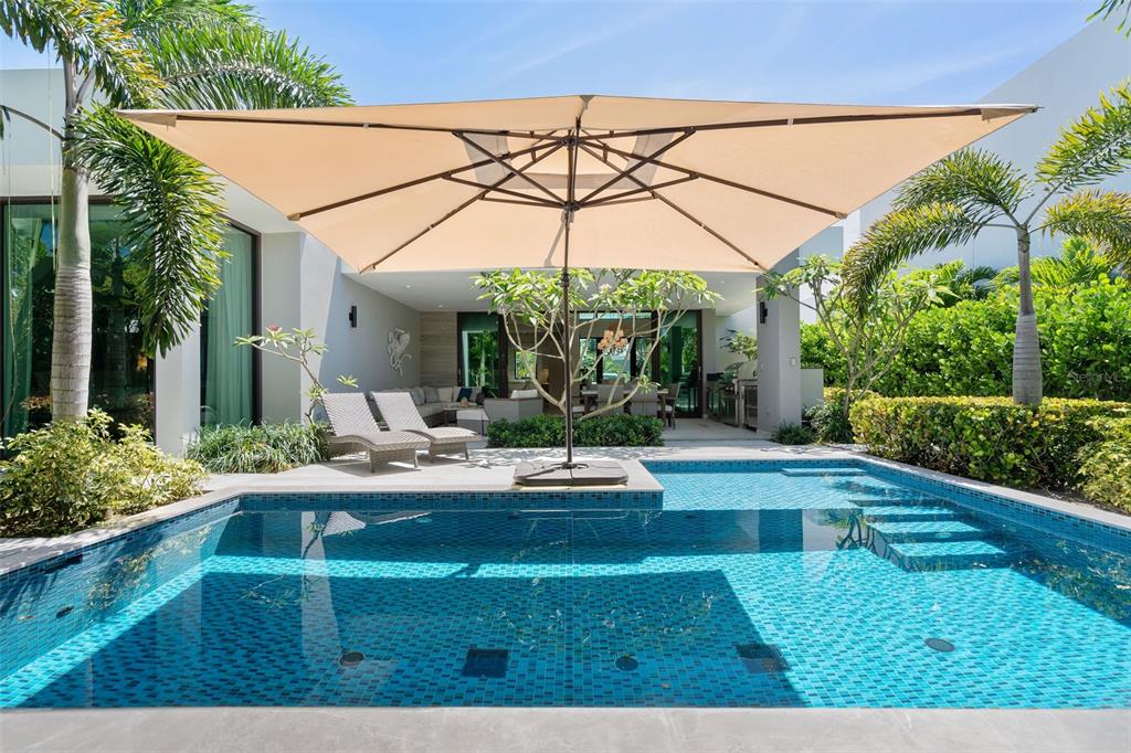 A swimming pool with a tan umbrella and lounge chairs sits outside a modern home — 32 THE ISLES, DORADO, PR