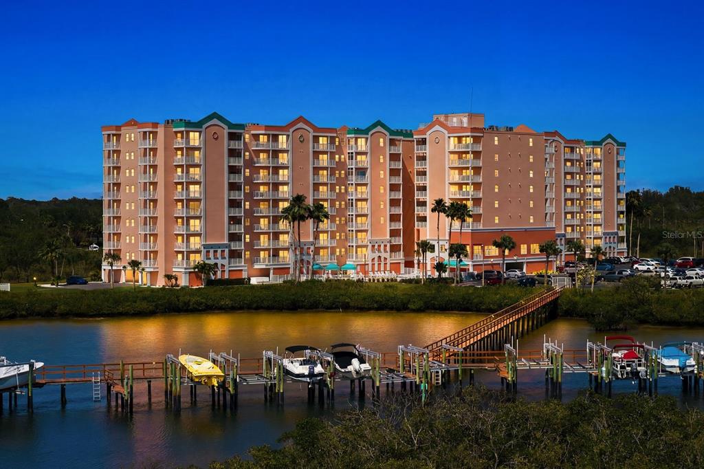 A multi-story waterfront apartment building with a wooden dock and several boats in the foreground — 4516 SEAGULL DRIVE UNIT 701, NEW PORT RICHEY, FL