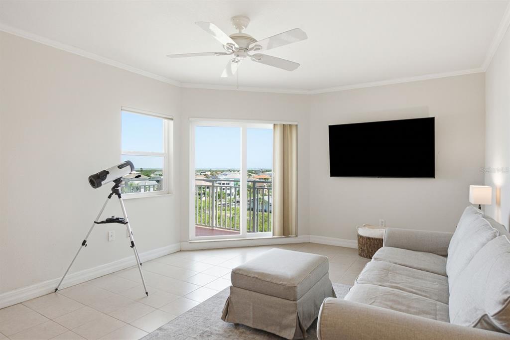 A living room features a sofa, ottoman, wall-mounted television, ceiling fan, and a telescope by the window — 4516 SEAGULL DRIVE UNIT 701, NEW PORT RICHEY, FL