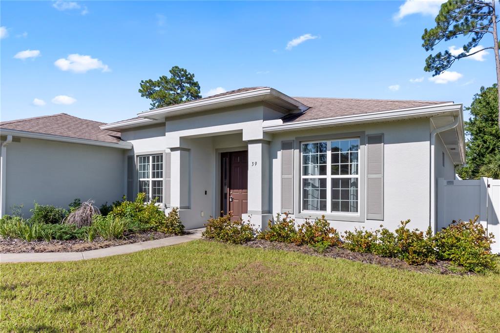 A single-story house with a beige stucco exterior, a brown front door, and landscaped yard — 39 BOULDER ROCK DRIVE, PALM COAST, FL