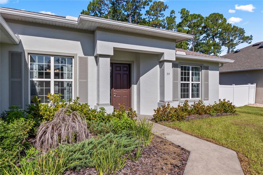 The exterior of a single-story house features a brown front door and a concrete walkway — 39 BOULDER ROCK DRIVE, PALM COAST, FL