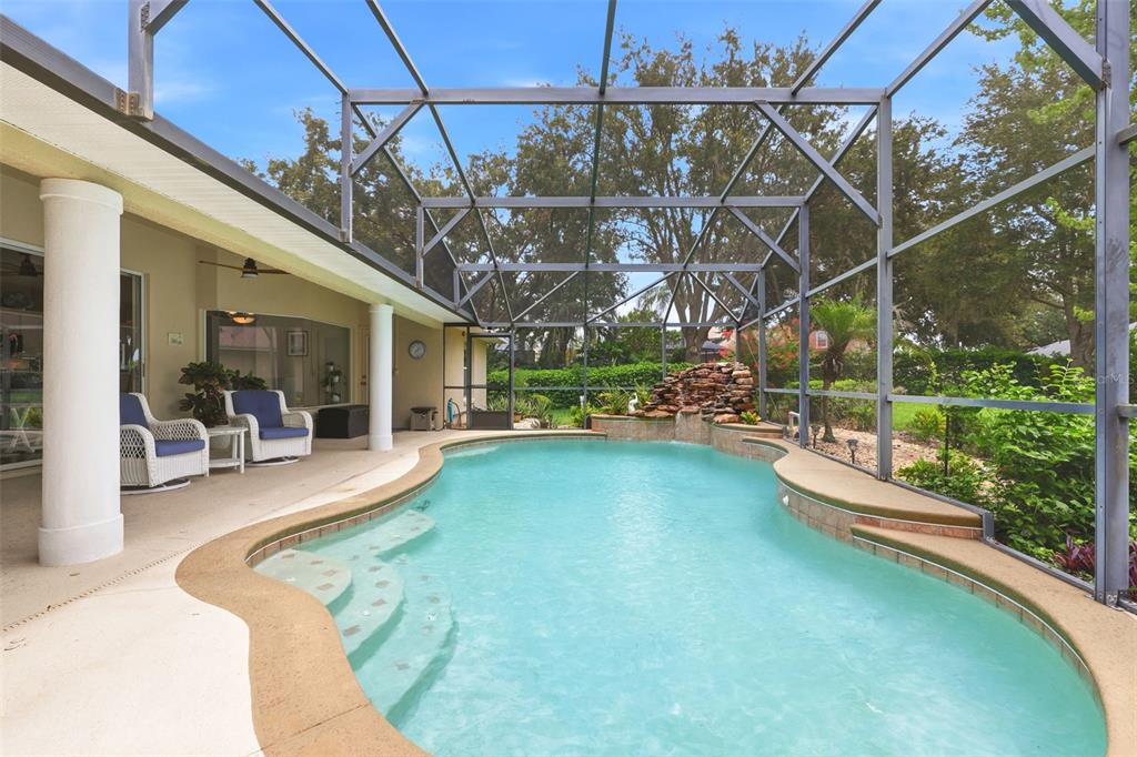 A screened-in patio features a swimming pool with a rock waterfall and lounge seating — 11310 SUSANS POINT DRIVE, CLERMONT, FL
