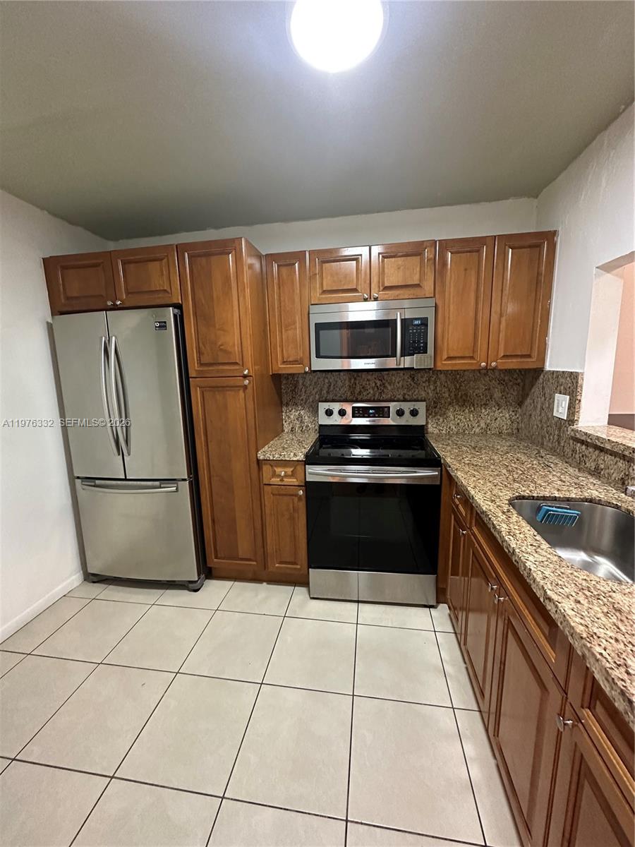 A kitchen features wood cabinets, granite countertops, stainless steel appliances, and light-colored floor tiles — 11279 SW 88th St # 210K, Miami FL 33176, MIAMI, FL