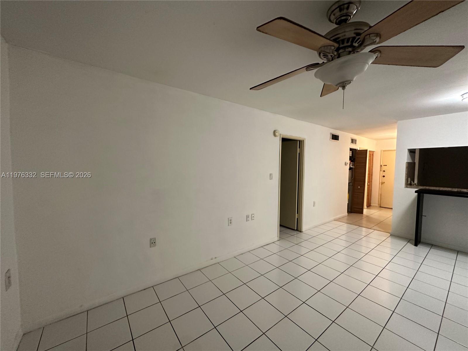 A white-walled room features a ceiling fan, tiled flooring, and an open kitchen pass-through — 11279 SW 88th St # 210K, Miami FL 33176, MIAMI, FL