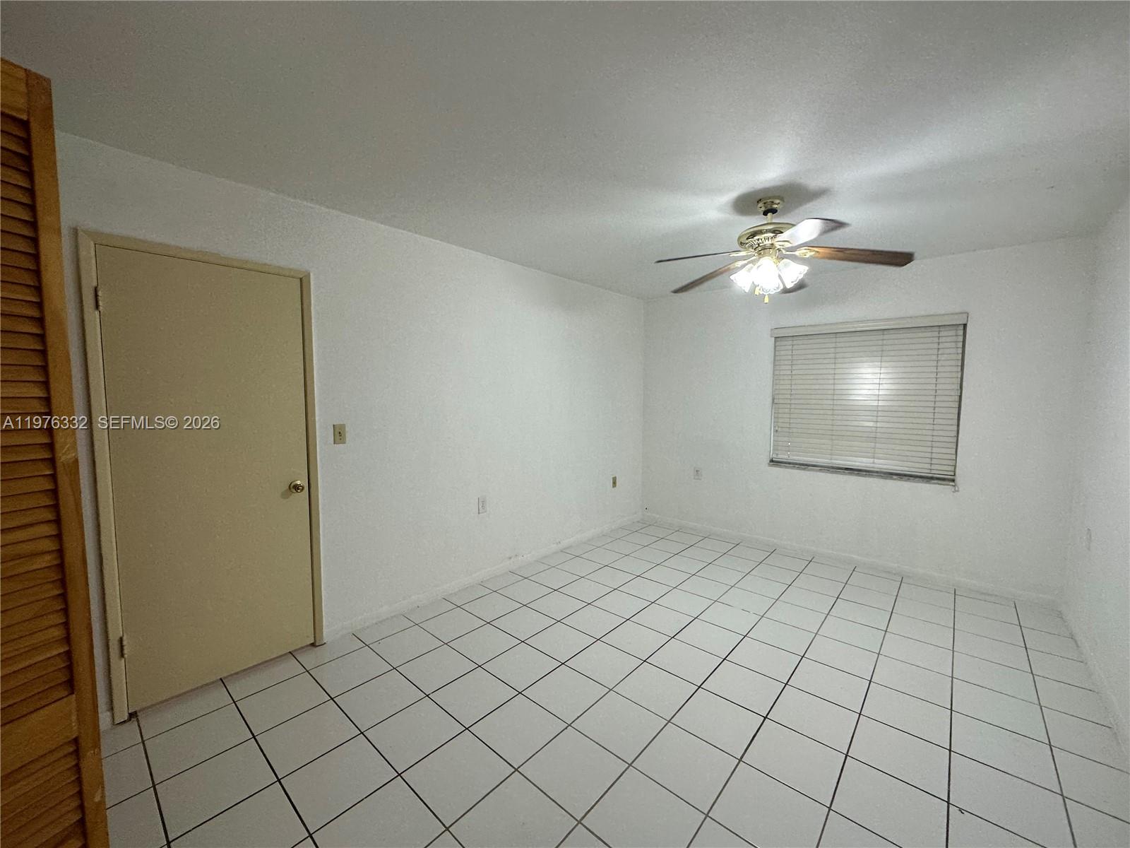 An empty room features white walls, white floor tiles, a ceiling fan, and a door — 11279 SW 88th St # 210K, Miami FL 33176, MIAMI, FL
