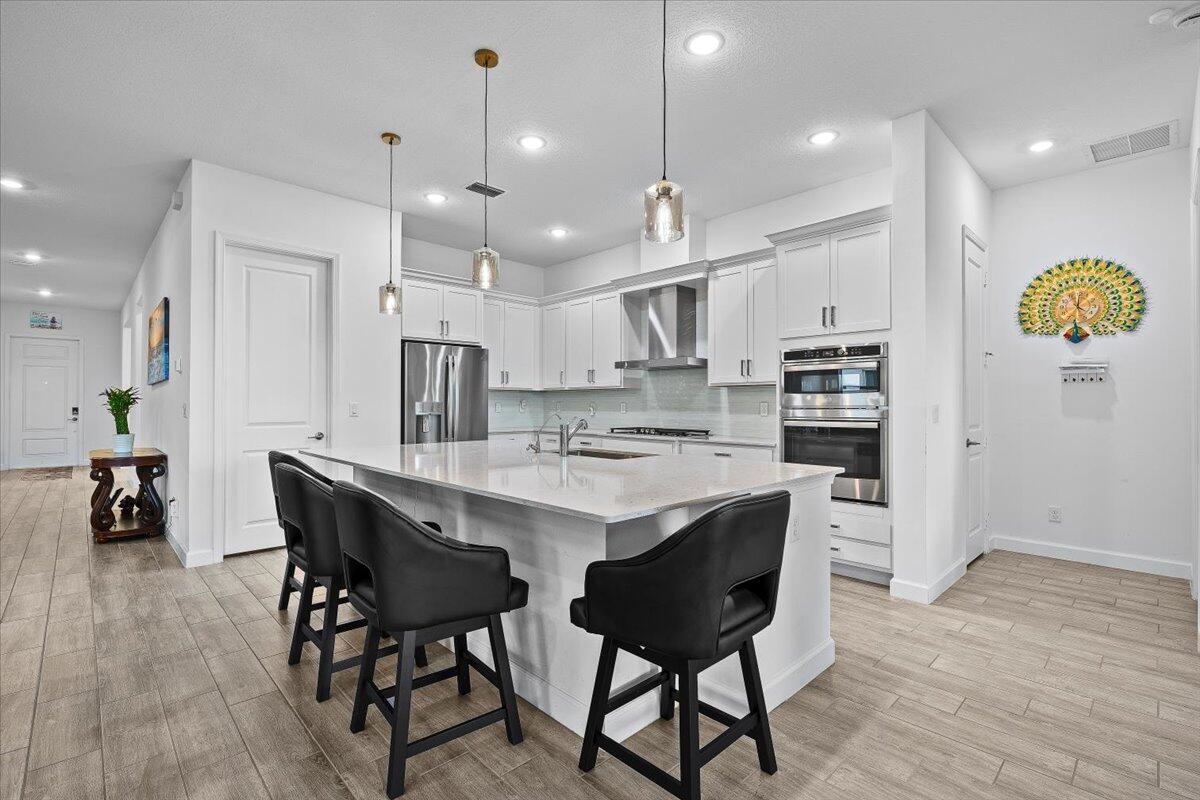 A modern kitchen features white cabinets, a large island with bar stools, and stainless appliances — 1130 Tangled Orchard Trace, FL 33470, FL