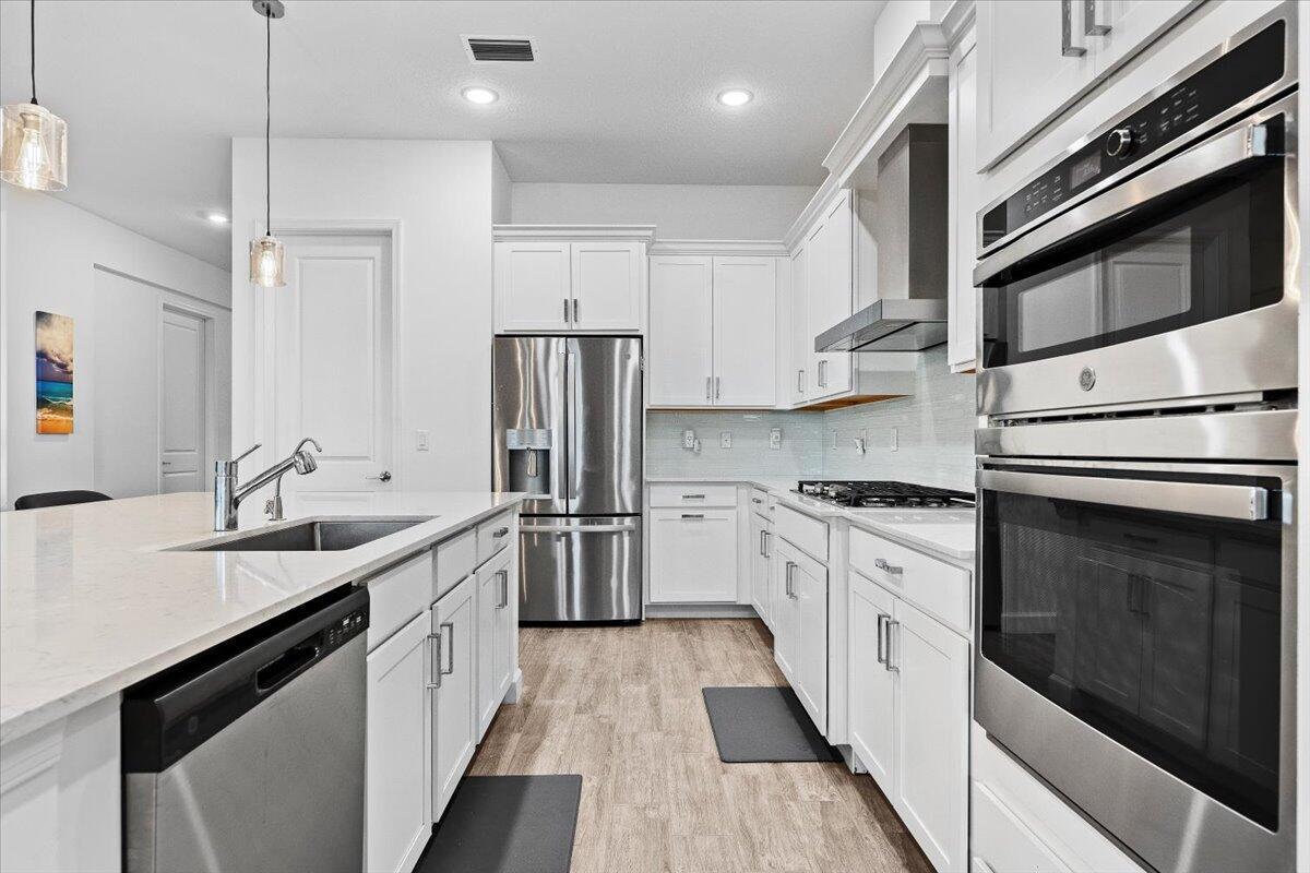 A modern kitchen features white cabinetry, stainless steel appliances, and a large quartz-topped island — 1130 Tangled Orchard Trace, FL 33470, FL