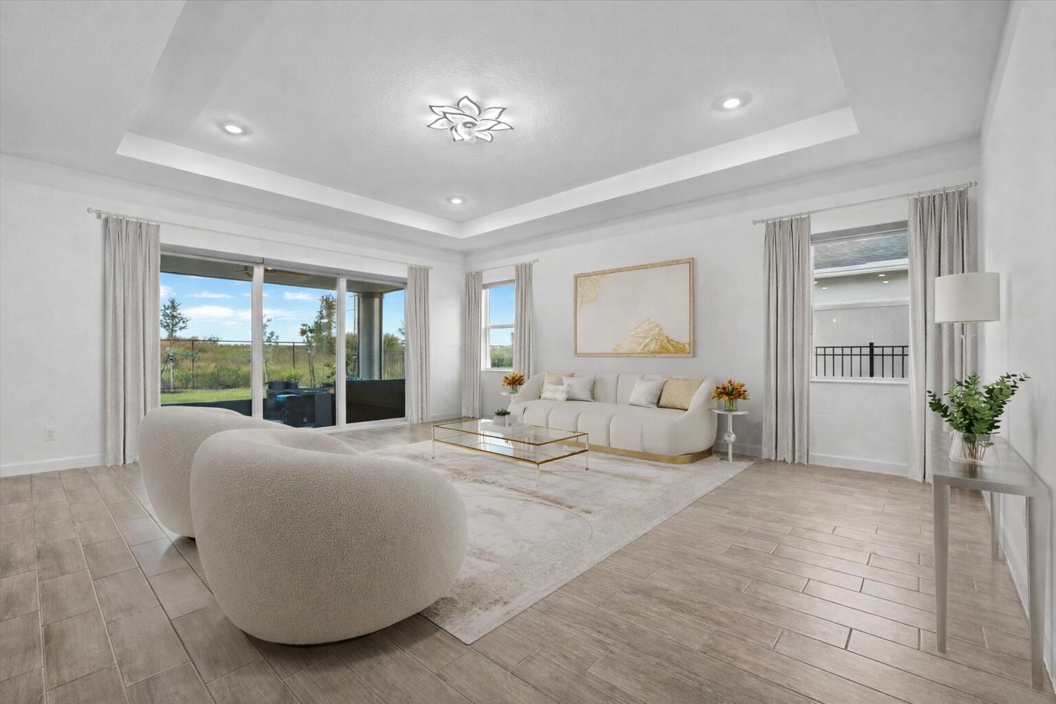 A bright living room features a tray ceiling, white walls, tile floors, and sliding glass doors — 1130 Tangled Orchard Trace, FL 33470, FL