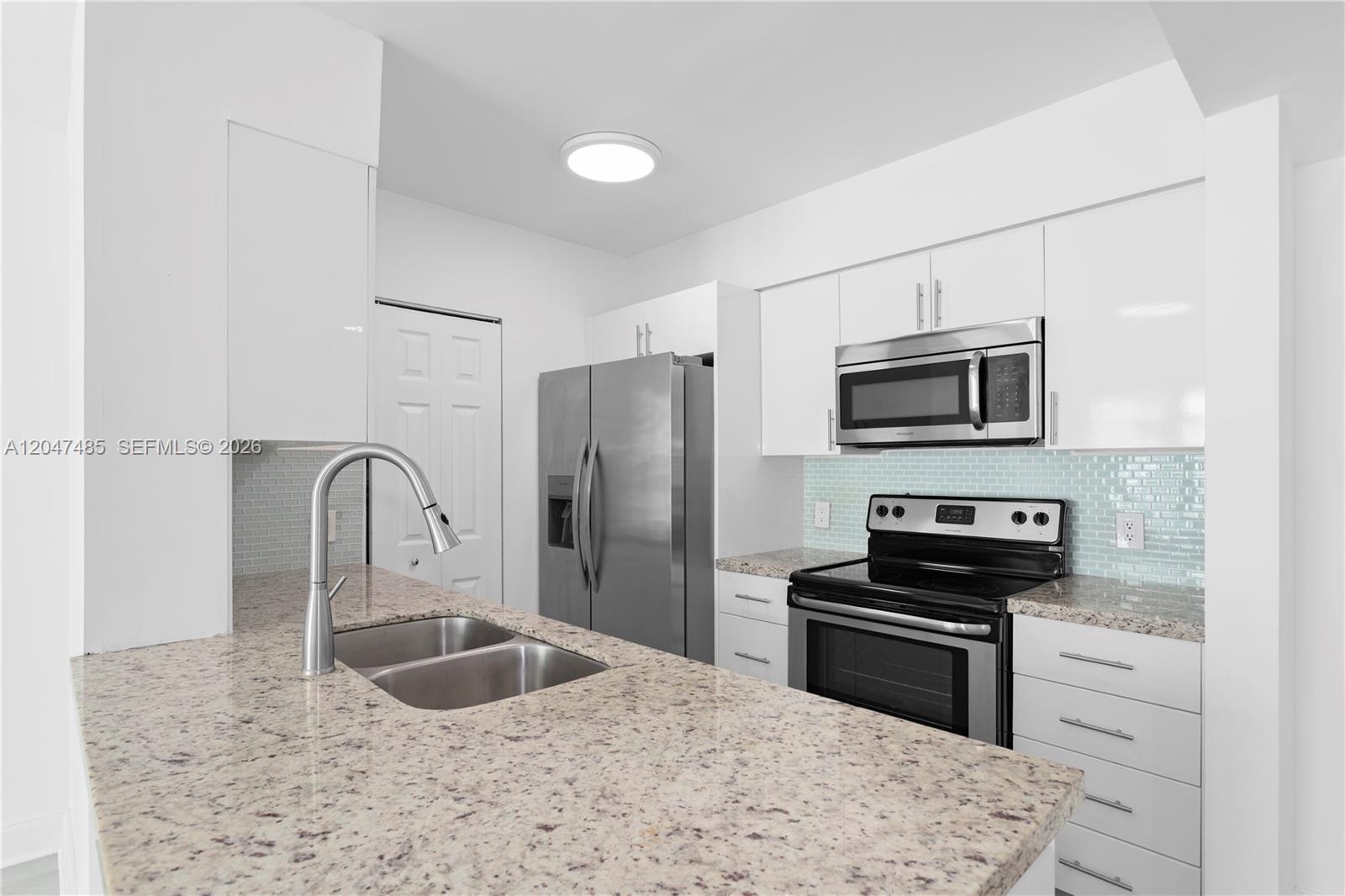 A kitchen features white cabinets, stainless steel appliances, granite countertops, and a light blue backsplash — 1155 Brickell Bay Dr # 2206, Miami FL 33131, MIAMI, FL