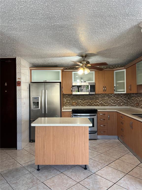 A kitchen features wood cabinets, stainless steel appliances, a center island, and tiled flooring — SB 30 LA MANSION, CATANO, PR