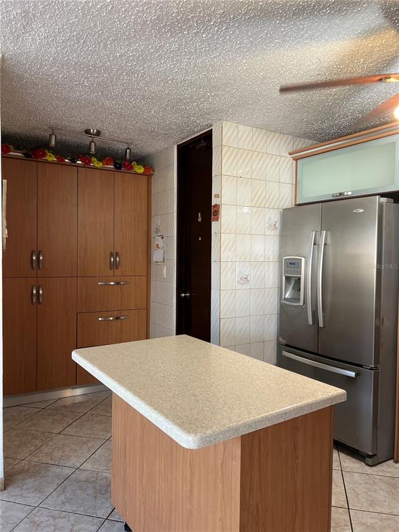 A kitchen features wood cabinets, a portable island, tile flooring, and a stainless steel refrigerator — SB 30 LA MANSION, CATANO, PR