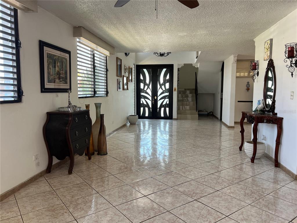 A spacious foyer features tiled floors, a decorative double front door, and a staircase — SB 30 LA MANSION, CATANO, PR