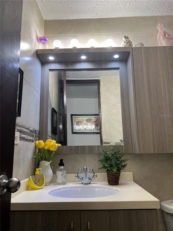 A bathroom vanity features a sink, mirror, wood-toned cabinetry, and decorative lighting — SB 30 LA MANSION, CATANO, PR