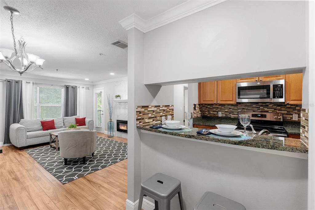 A kitchen with granite countertops and wood cabinets overlooks a living room with a fireplace — 11901 4TH STREET N UNIT 8207, ST PETERSBURG, FL