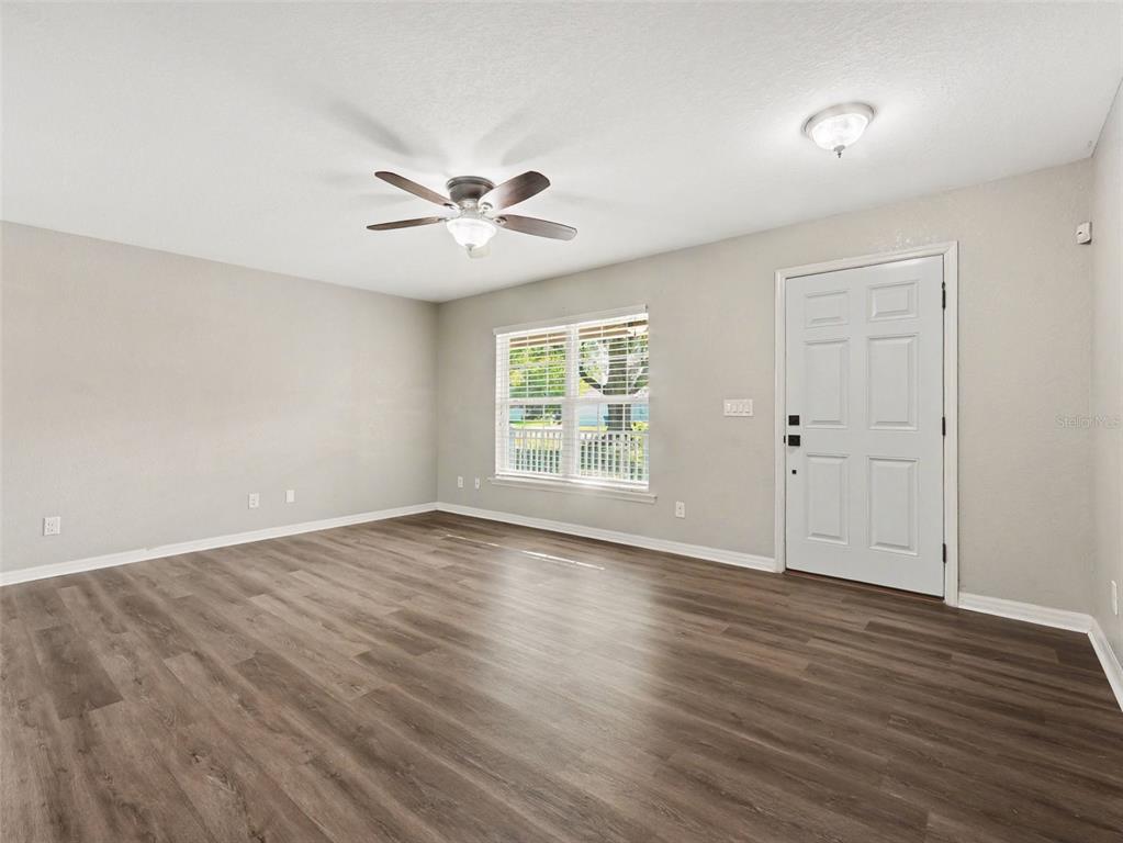 An empty living room features light gray walls, wood-look flooring, a ceiling fan, and a door — 410 NE 12TH AVENUE, MULBERRY, FL