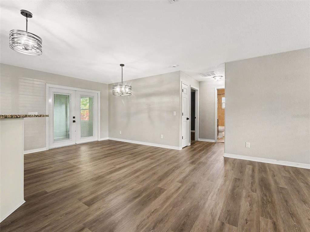 An empty room with wood-look flooring, two pendant lights, and glass doors leading outside — 410 NE 12TH AVENUE, MULBERRY, FL