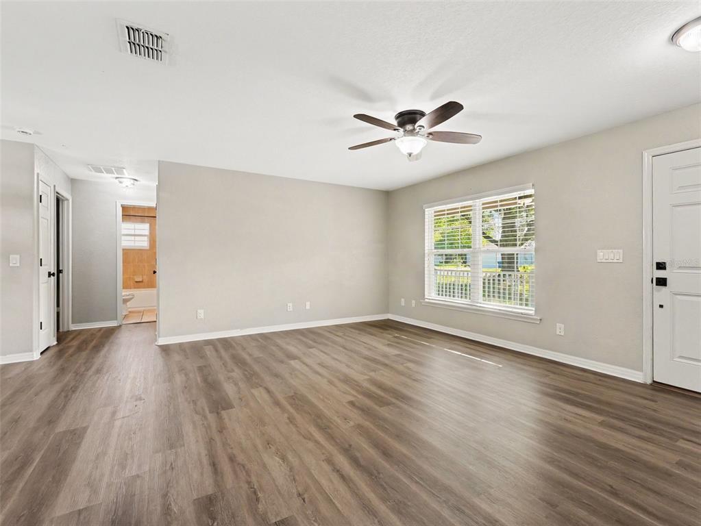 An empty living room features light gray walls, wood-look flooring, a ceiling fan, and windows — 410 NE 12TH AVENUE, MULBERRY, FL