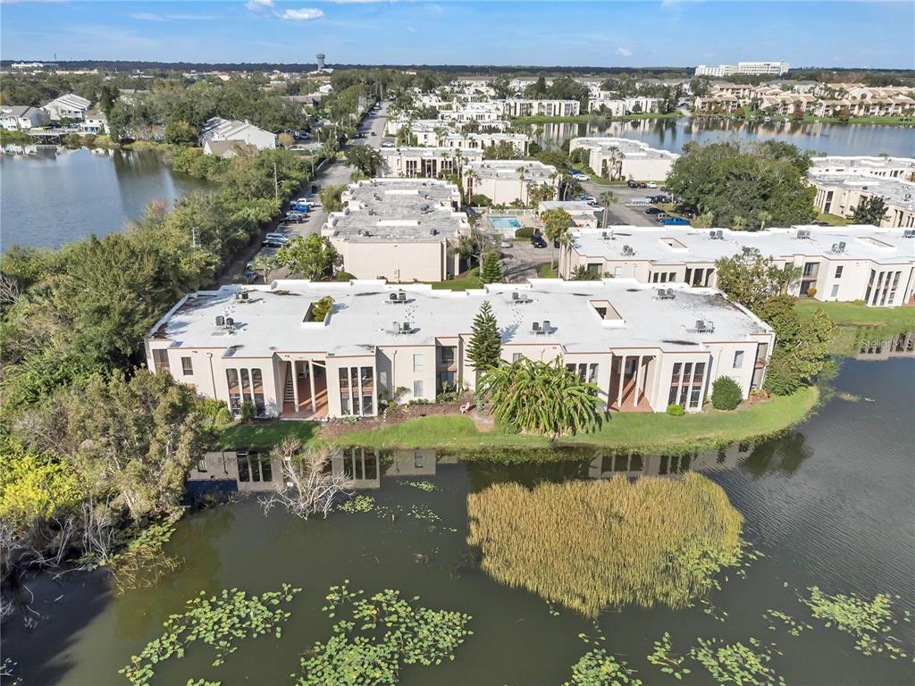 An aerial view shows a multi-story apartment complex situated along a lake with vegetation — 542 ORANGE DRIVE UNIT 26, ALTAMONTE SPRINGS, FL