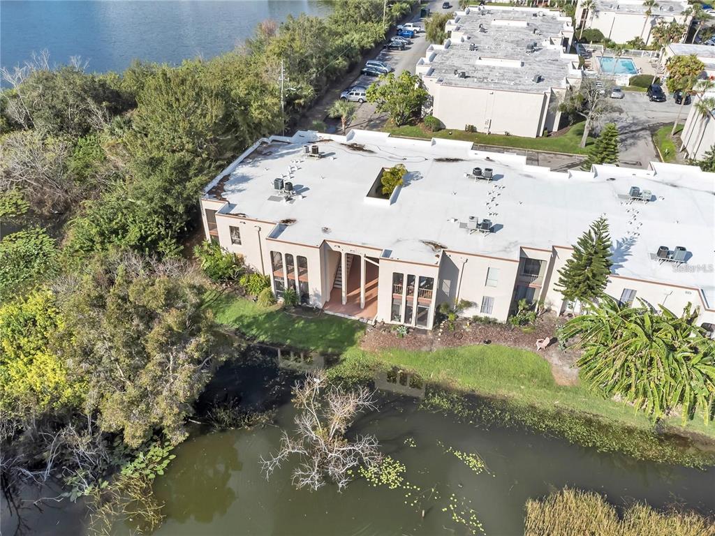 An aerial view shows a multi-story apartment building situated next to a pond and trees — 542 ORANGE DRIVE UNIT 26, ALTAMONTE SPRINGS, FL