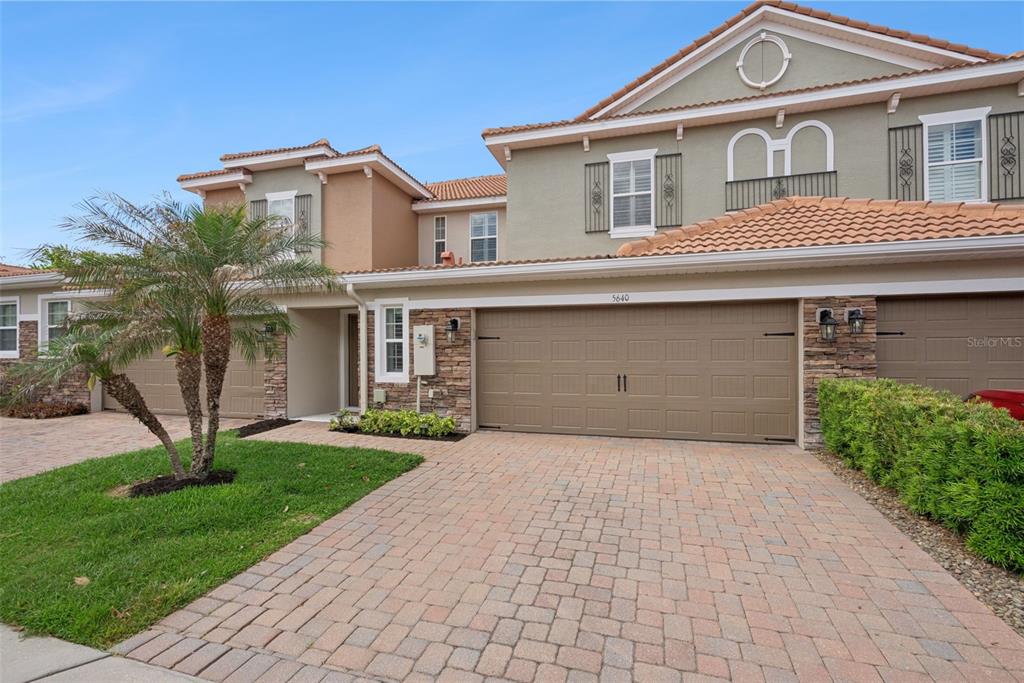 A two-story townhouse features a tan stucco exterior, a stone-accented facade, and a paved driveway — 5640 SIRACUSA LANE, SANFORD, FL