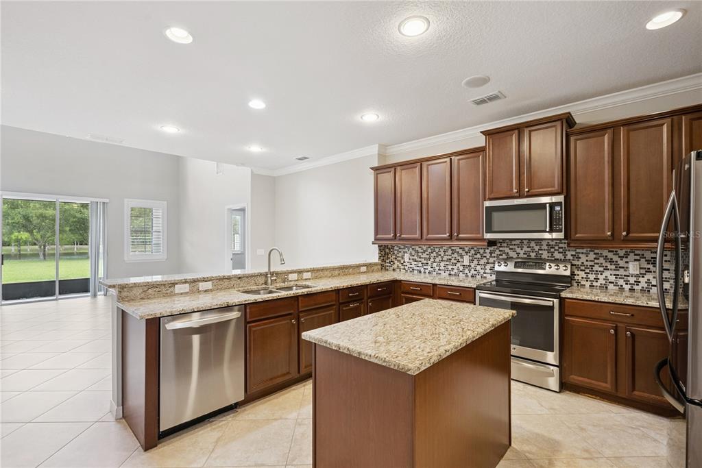 A kitchen features dark wood cabinets, granite countertops, stainless steel appliances, and a center island — 5640 SIRACUSA LANE, SANFORD, FL