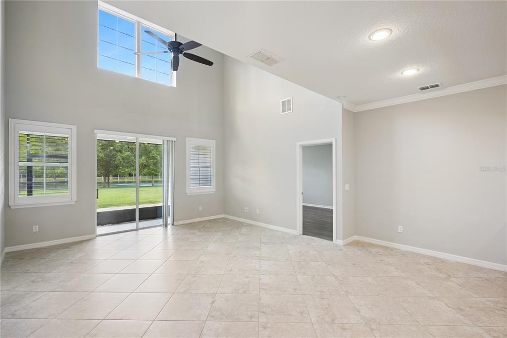 A bright living room features high ceilings, tile flooring, a ceiling fan, and sliding glass doors — 5640 SIRACUSA LANE, SANFORD, FL