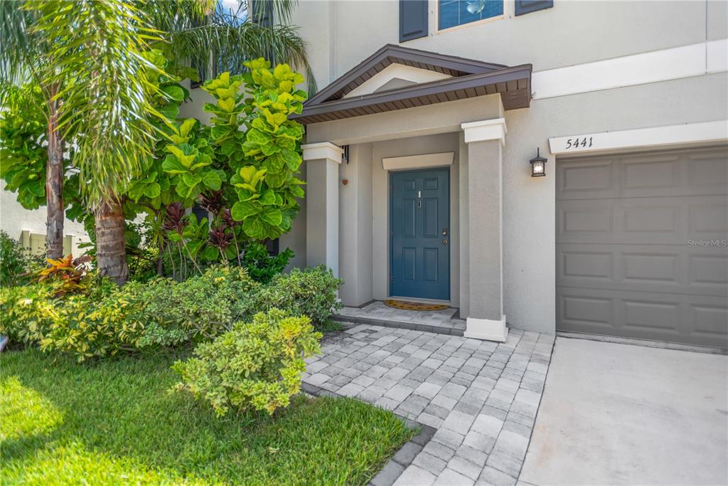 The exterior of a two-story home features a blue front door, a paved walkway, and landscaping — 5441 RAINWOOD MEADOWS DRIVE, APOLLO BEACH, FL