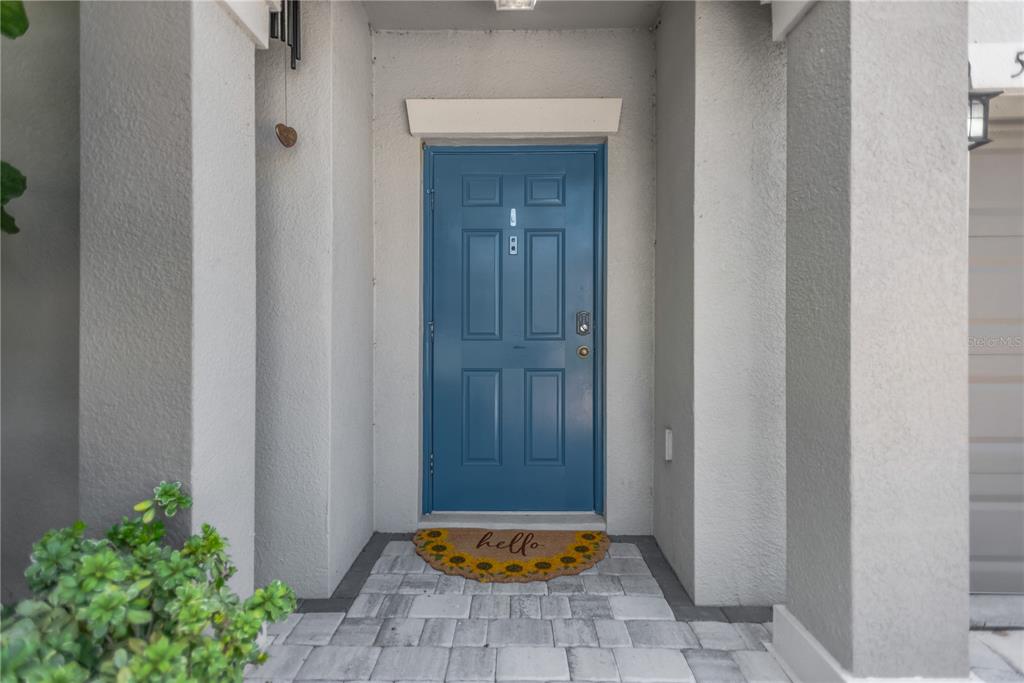 A blue front door with a sunflower welcome mat sits between two gray pillars — 5441 RAINWOOD MEADOWS DRIVE, APOLLO BEACH, FL