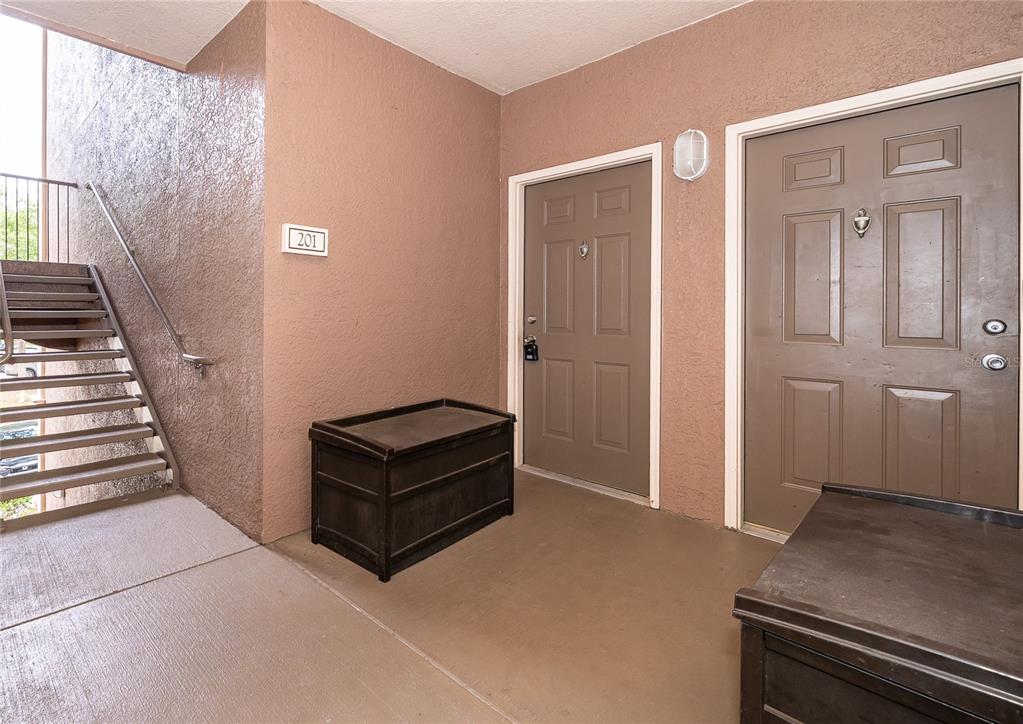An outdoor apartment landing features two brown doors, a staircase, and two storage chests — 6141 METROWEST BOULEVARD UNIT 201, ORLANDO, FL