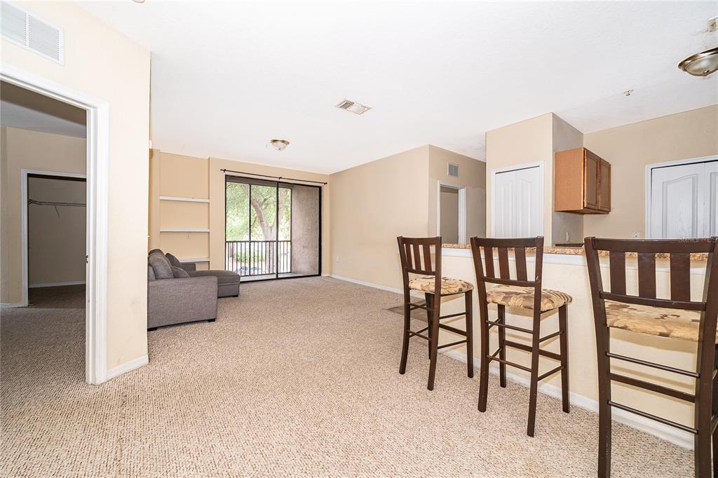 A carpeted living room features a breakfast bar with three stools and a sliding glass door — 6141 METROWEST BOULEVARD UNIT 201, ORLANDO, FL