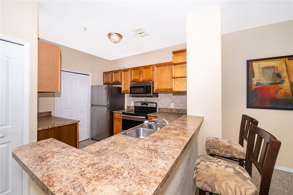 A kitchen with wood cabinets, stainless steel appliances, and a breakfast bar with two chairs — 6141 METROWEST BOULEVARD UNIT 201, ORLANDO, FL