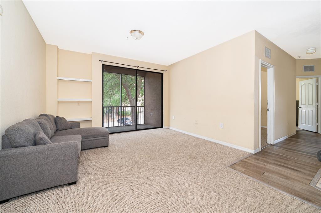 A living room features beige carpet, a gray sectional sofa, built-in shelves, and a sliding door — 6141 METROWEST BOULEVARD UNIT 201, ORLANDO, FL