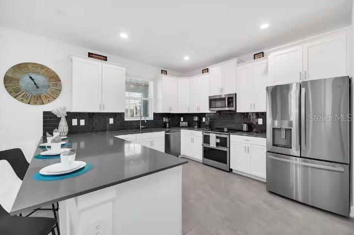 A modern kitchen features white cabinets, stainless steel appliances, a dark island, and black backsplash — 9092 SOMMERSET HILLS DRIVE, DAVENPORT, FL