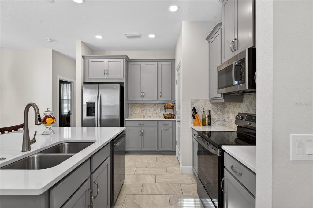 A modern kitchen features gray cabinets, stainless steel appliances, and a white quartz island countertop — 1192 VIA GALUPPI STREET, KISSIMMEE, FL