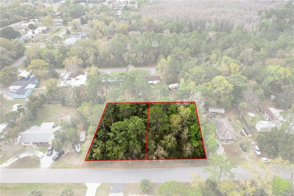 An aerial view shows two adjacent, wooded, rectangular lots outlined in red along a road — 7636 W SUNBURST LANE, HOMOSASSA, FL