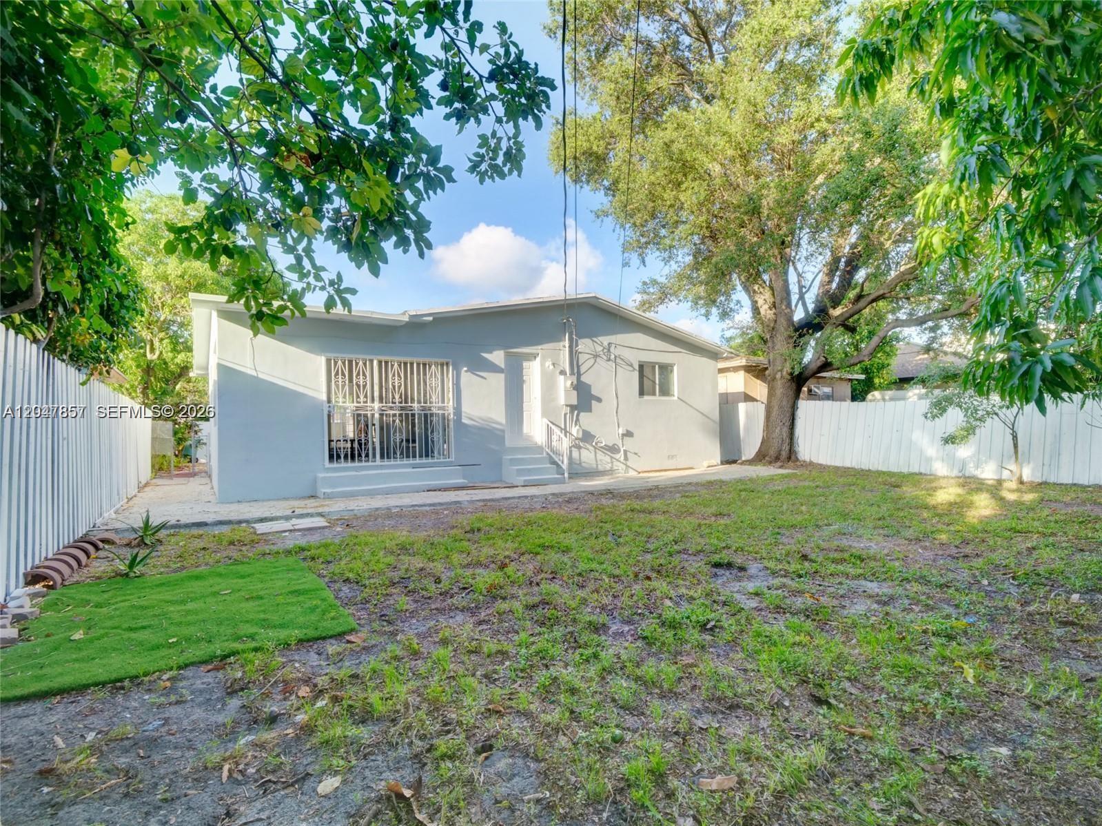 The exterior of a light blue house features a fenced backyard with a large tree — 1141 NW 75th St, Miami FL 33150, MIAMI, FL